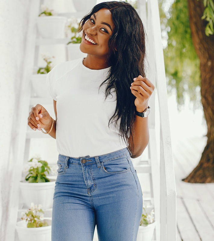 Cute black girl near white wall. Lady in a white t-shirt and blue jeans. Woman with watch - Arm Lift